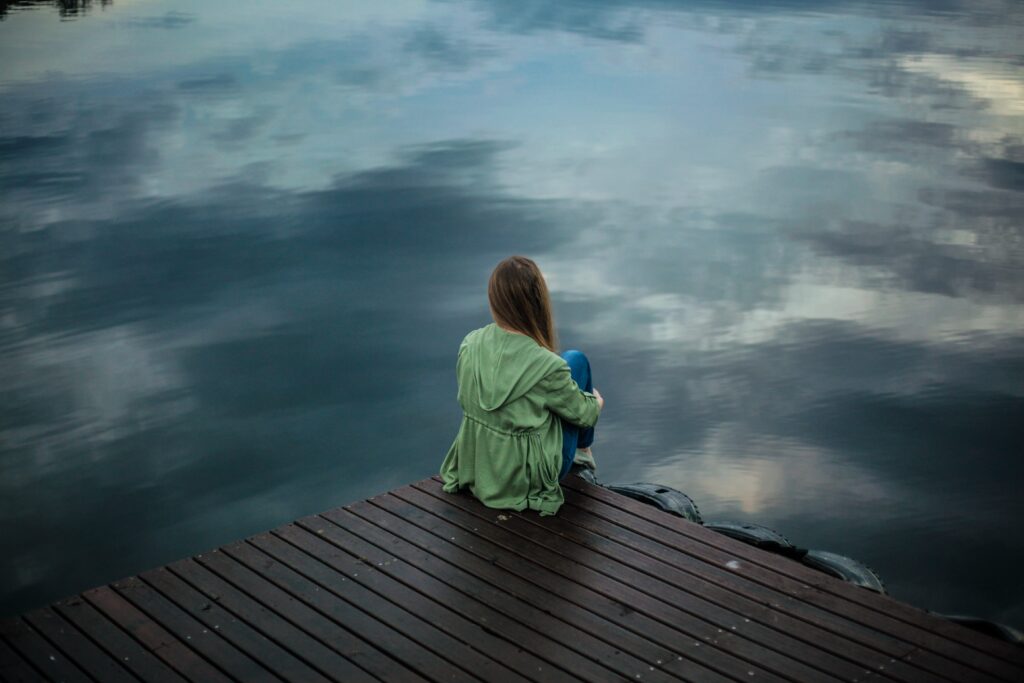 A woman sitting on the edge of a deck above a body of water.